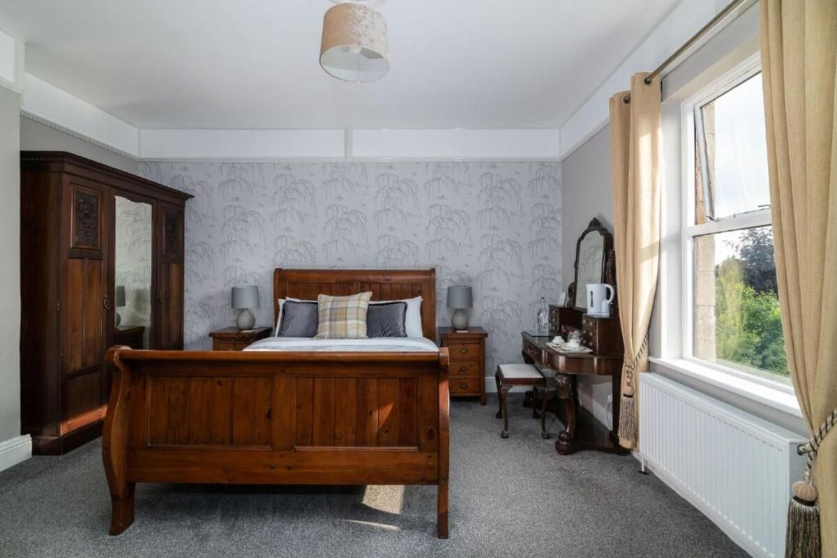 Un dormitorio con cama de madera, mesitas de noche, cómoda, espejo y ventana con cortinas.
