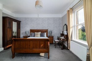 Un dormitorio con cama de madera, mesitas de noche, cómoda, espejo y ventana con cortinas.