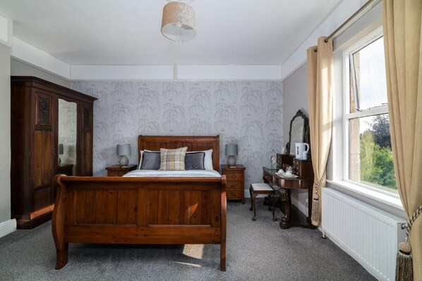 Un dormitorio con cama de madera, mesitas de noche, cómoda, espejo y ventana con cortinas.