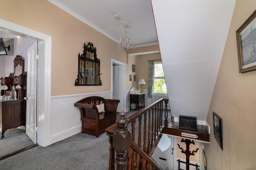 A hallway with a wooden staircase, a mirror, a chandelier, and a door leading to another room.