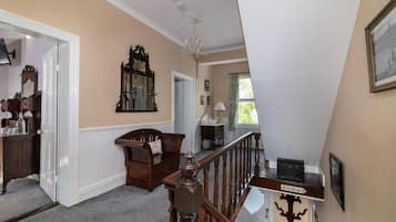 A hallway with a wooden staircase, a mirror, a chandelier, and a door leading to another room.