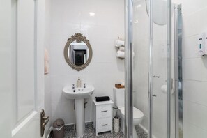 Un baño con lavamanos blanco, espejo, inodoro y ducha con cerramiento de vidrio.