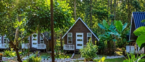 A wooden cabin with a porch, surrounded by lush greenery and trees.