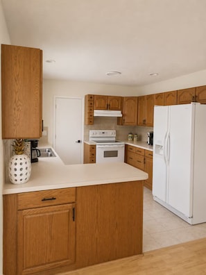 A kitchen with wooden cabinets, a white countertop, a stove, a refrigerator, and a pineapple decoration.