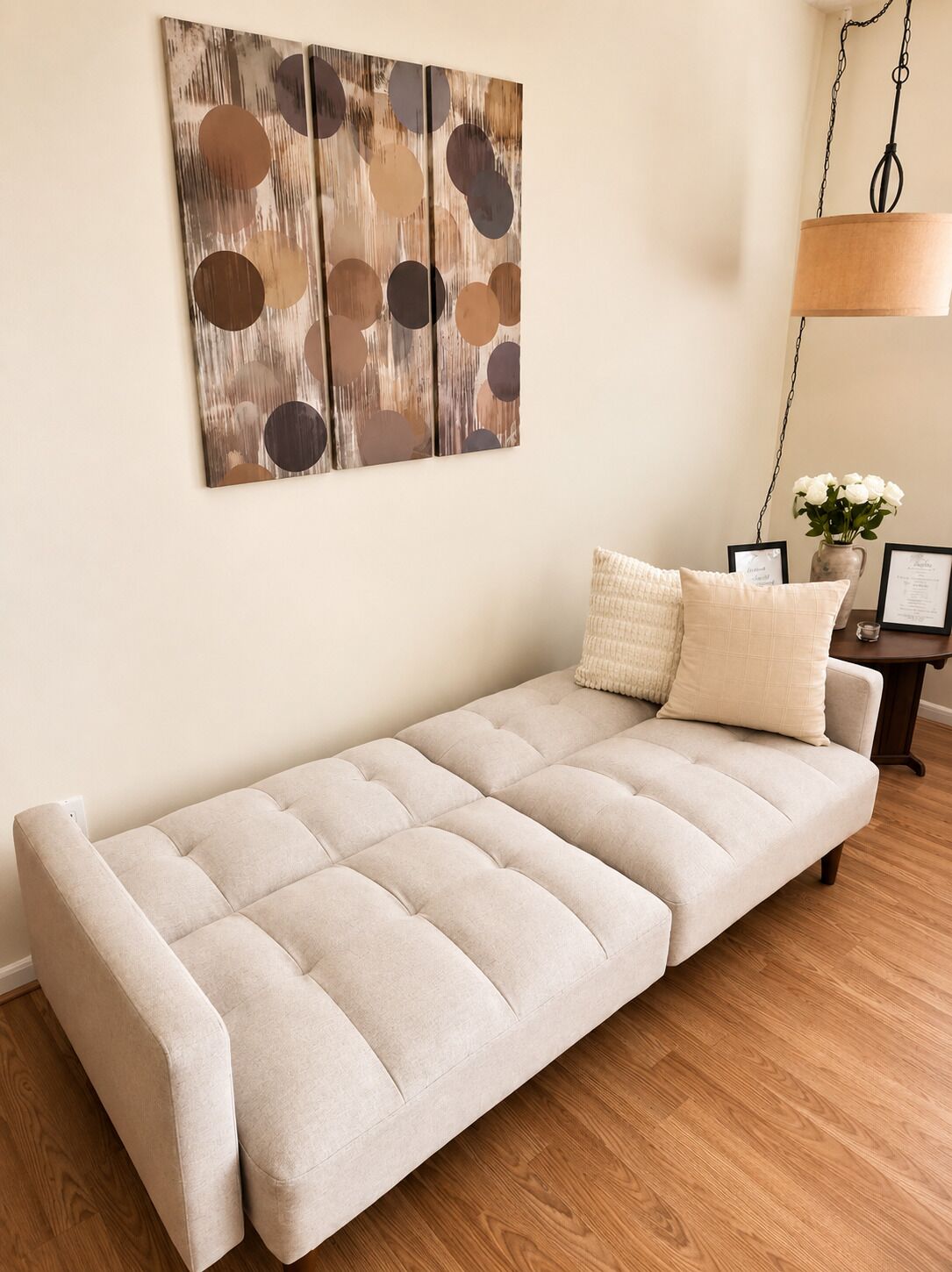 Un canapé avec un coussin, un tableau abstrait accroché au mur et une lampe suspendue.