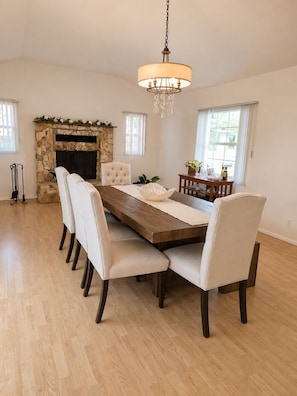 A dining room with a stone fireplace, a chandelier, and a wooden table with chairs.