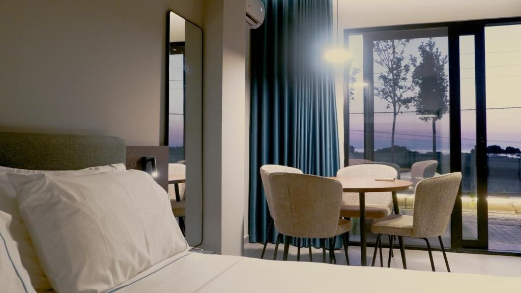 Una habitación de hotel con cama, una mesa de comedor con sillas y un ventanal con vistas al exterior.