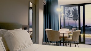 A hotel room with a bed, a dining table with chairs, and a large window with a view of the outdoors. - Eden Hotel Spille (Rrogozhine)