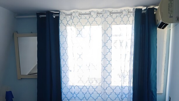 Um quarto com cama, mesa de cabeceira, espelho e janela com cortinas.
