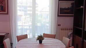 Uma sala de jantar com uma mesa redonda, seis cadeiras, uma planta em vaso e vista através de uma janela grande.