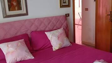 Ein Bett mit einer rosa Tagesdecke, zwei Kissen und einem zusammengerollten Handtuch sowie einer Tube Creme.