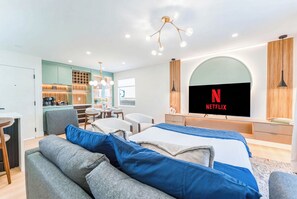 Quarto de hotel moderno com uma cama grande, uma escrivaninha e uma cozinha compacta.