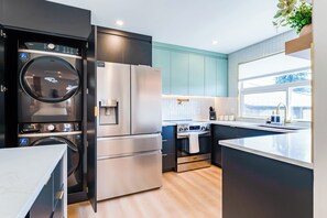 A modern kitchen with a built-in washer and dryer, a stainless steel refrigerator, and an oven. - Luxury Designer Home with Spa Bathrooms • King Bed • AC • Minutes to Downtown (Calgary)