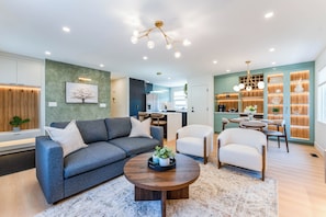 A modern living room with a sofa, chairs, a coffee table, and a kitchen in the background.