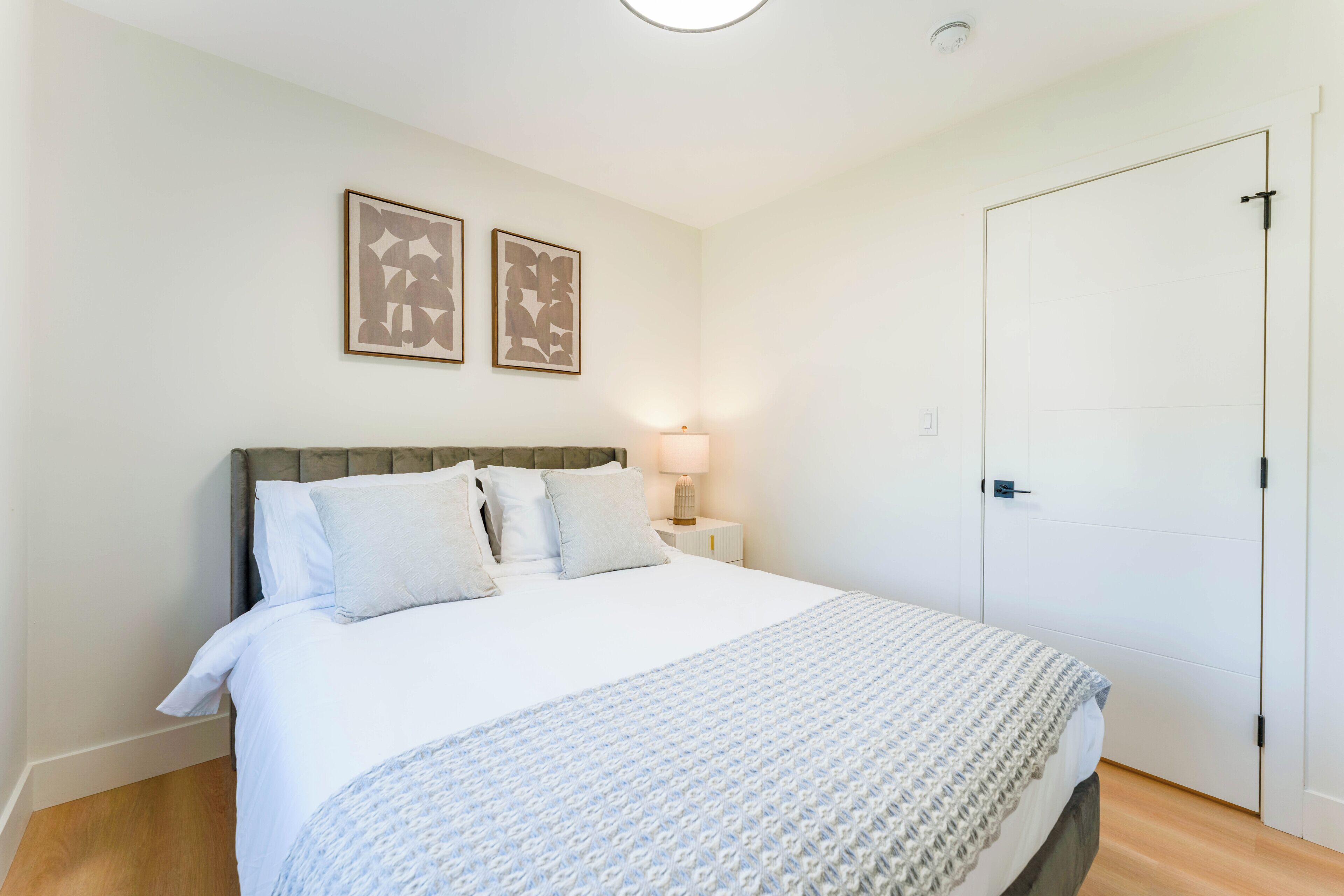 A bedroom with a bed, a nightstand, a lamp, and two framed pictures on the wall.