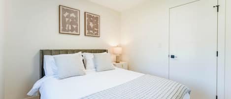 A bedroom with a bed, a nightstand, a lamp, and two framed pictures on the wall.