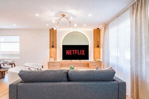 Una sala de estar moderna con un sofá gris, un televisor de pantalla plana que muestra 'NETFLIX' y un mueble de madera.