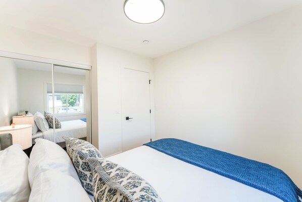 A bedroom with a bed, a bedside table, a lamp, a mirror, and a door.