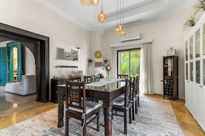 Comedor con una mesa grande y sillas, una lámpara de araña y vistas a follaje exterior.
