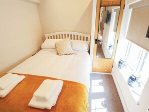 A neatly made bed with pillows and folded towels, a wooden headboard, and a window with curtains.