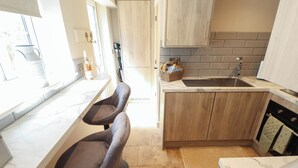 A kitchen with two bar stools, a sink, wooden cabinets, and a marble countertop. - Bee Hive Hut (King's Lynn)