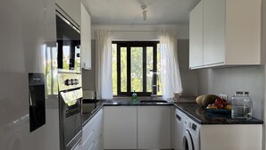 Een moderne keuken met een ingebouwde oven, een wasmachine en een raam met gordijnen.