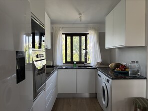 Eine moderne Küche mit Einbauofen, Waschmaschine und einem fenster mit Vorhängen.