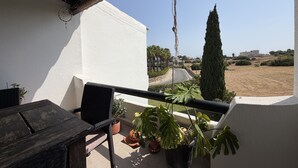 Een balkon met uitzicht op een weg en verre gebouwen, een bloempot en een houten tafel.