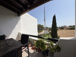 Ein Balkon mit Blick auf eine Straße und entfernte Gebäude, eine Topfpflanze und ein Holztisch.
