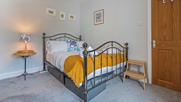A bedroom with a bed, a bedside table, a small stool, and a door. - Charming 2-Bed Home Away from Home in Nantwich (Cheshire East)