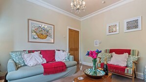A living room with a sofa, a wooden chest, and a vase with flowers. - Charming 2-Bed Home Away from Home in Nantwich (Cheshire East)