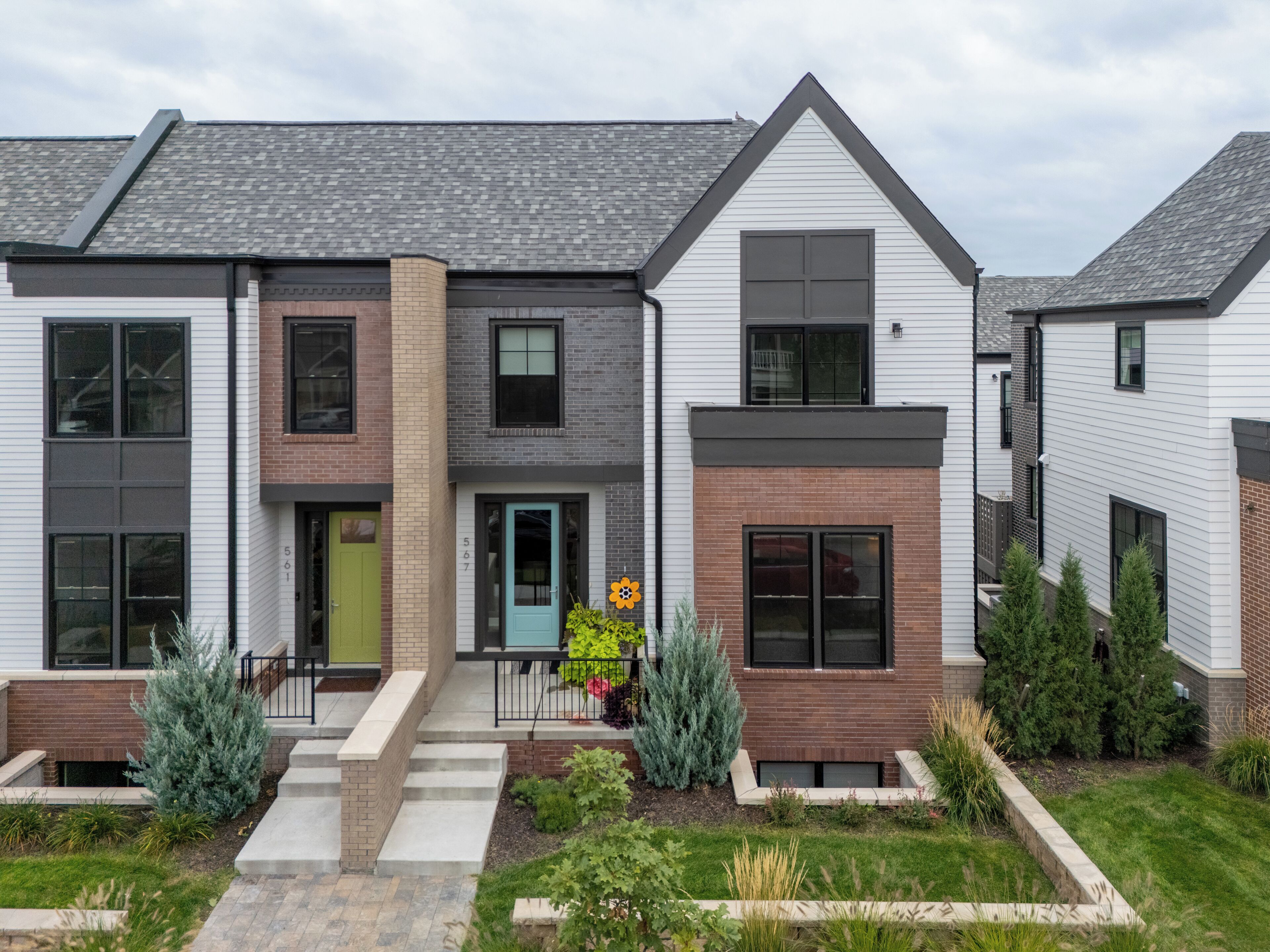 A modern two-story residential building with a brick facade, large windows, and a well-maintained lawn.