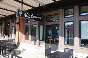 An exterior of a building with a sign reading '402 Creamery' and a neon 'OPEN' sign. There are outdoor tables and chairs.