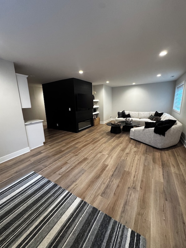 A modern living room with a sectional sofa, a flat-screen TV, and a wooden floor.