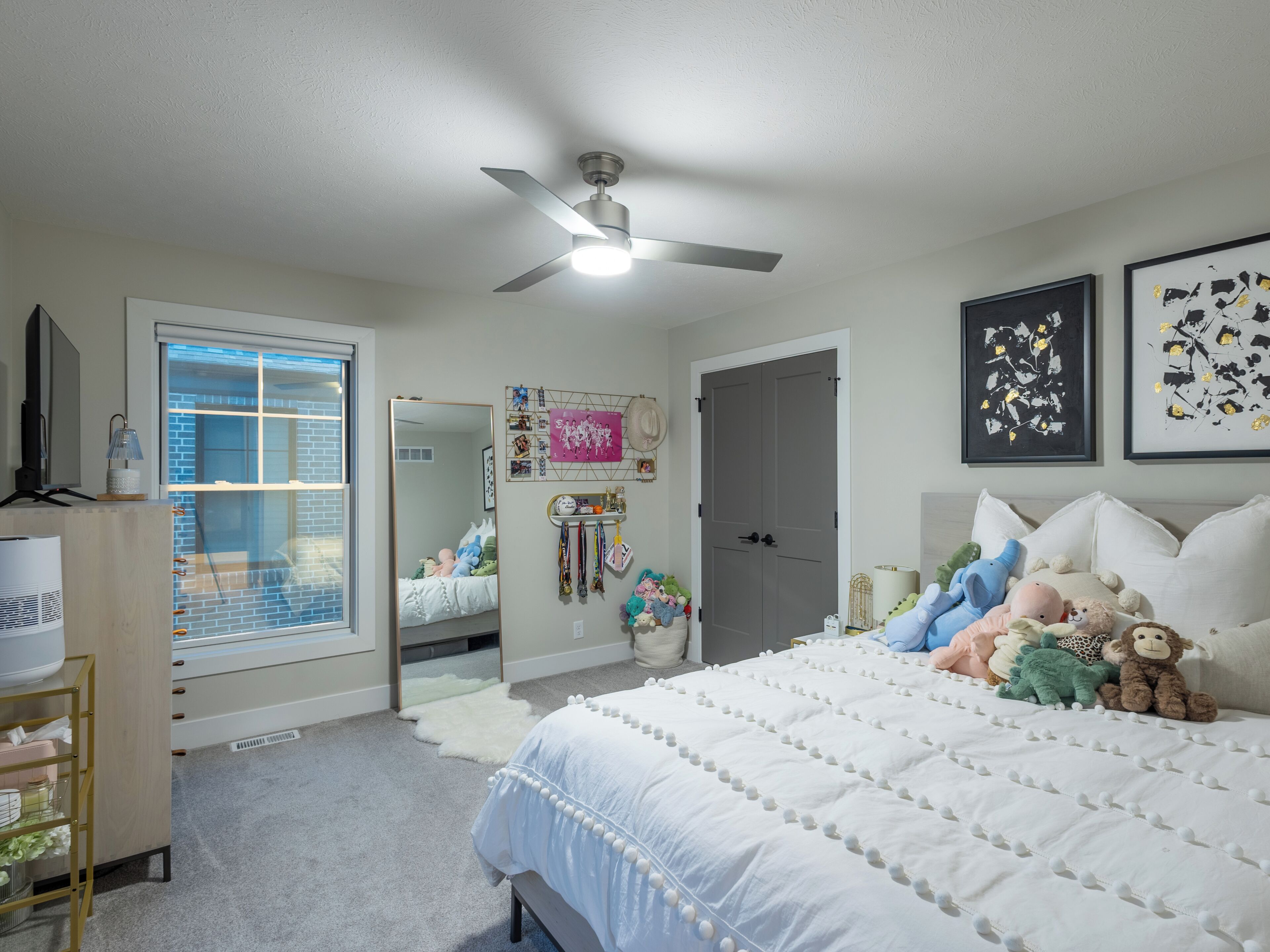 Une chambre à coucher avec un lit, un ventilateur de plafond, une commode, un miroir et une porte.