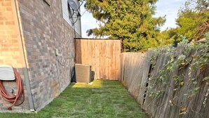 A backyard with a wooden fence, a brick wall, and a hose on the left. - Spacious Lakefront Retreat House with 1100sqft Sports Bar Patio & Hot Tub Near Little Elm Beach, Little Elm, Texas (Little Elm)