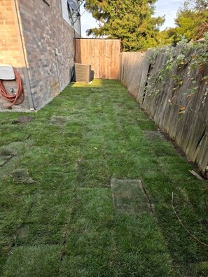 Ein Garten mit Holzzaun, einer Ziegelwand und einem Gartenschlauch auf der linken Seite.
