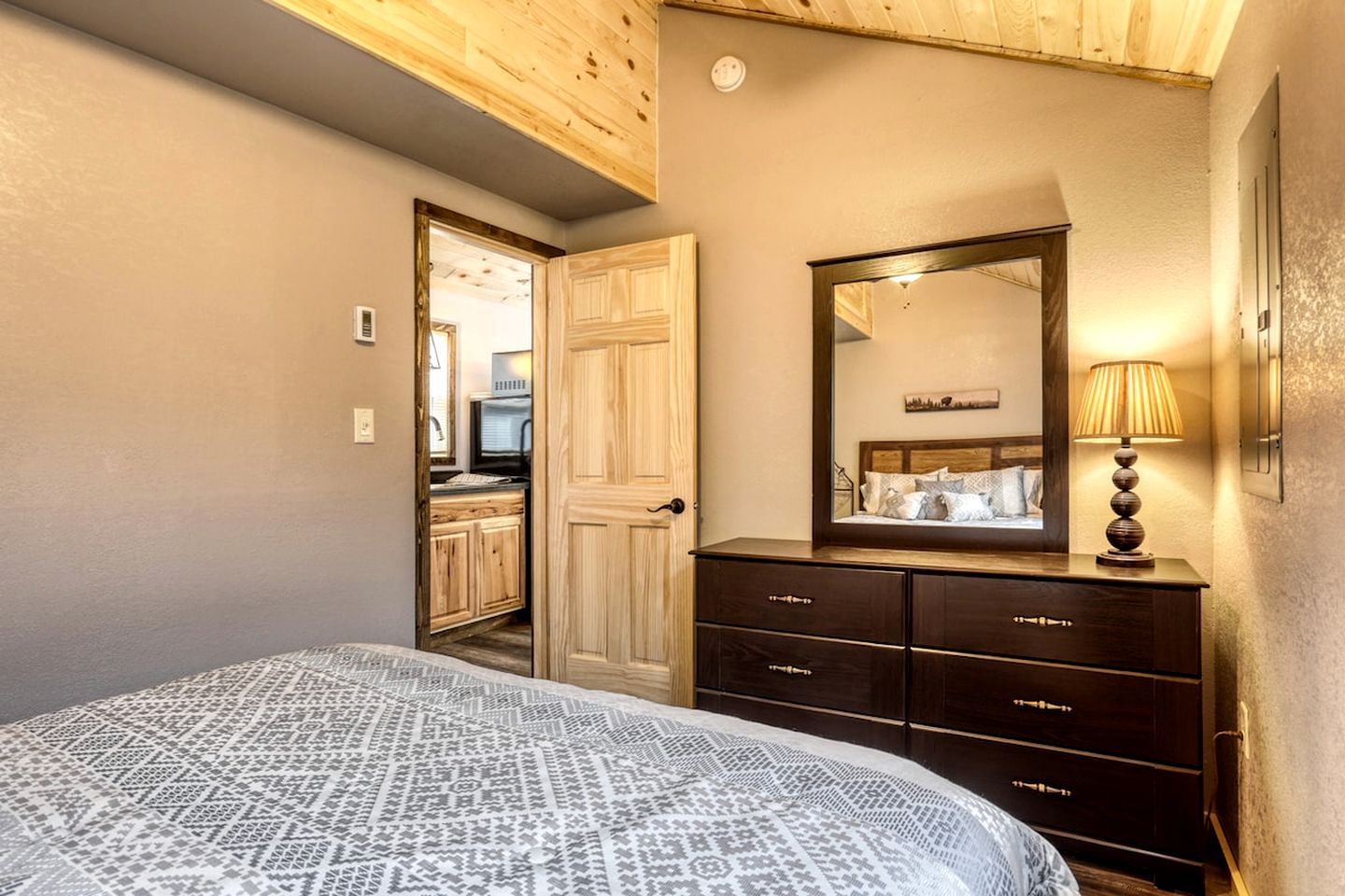 A bedroom with a bed, a dresser, a mirror, and a lamp.
