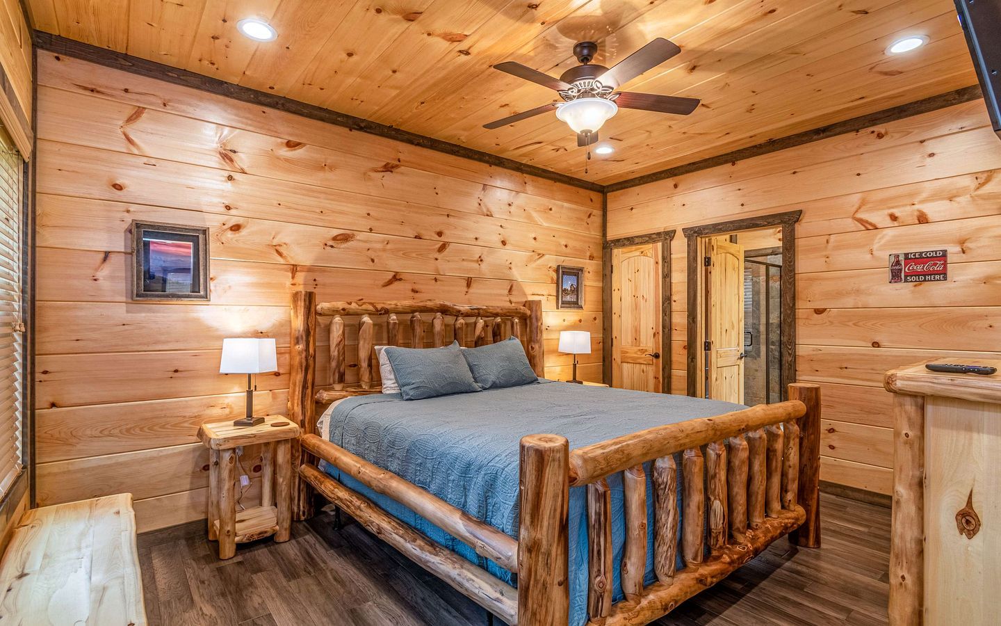A wooden cabin bedroom with a bed, two bedside tables, a ceiling fan, and a door.