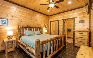 Quarto de cabana de madeira com cama, abajures, ventilador de teto e cômoda de madeira.