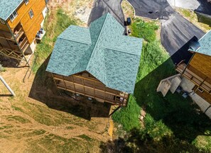 Uma cabana de madeira com telhado verde, rodeada por terreno gramado e uma estrada pavimentada.