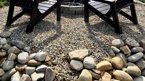Un espace recouvert de gravier, avec quatre chaises Adirondack disposées autour d’un foyer, le tout entouré d’un muret en pierre.