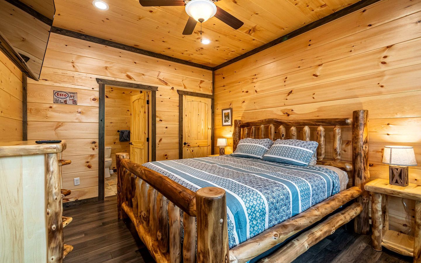 A wooden cabin bedroom with a bed, a nightstand, a ceiling fan, and a door.
