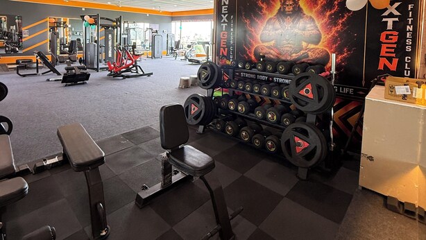 Un gimnasio con equipamiento para levantamiento de pesas, bancos y un cartel motivacional.