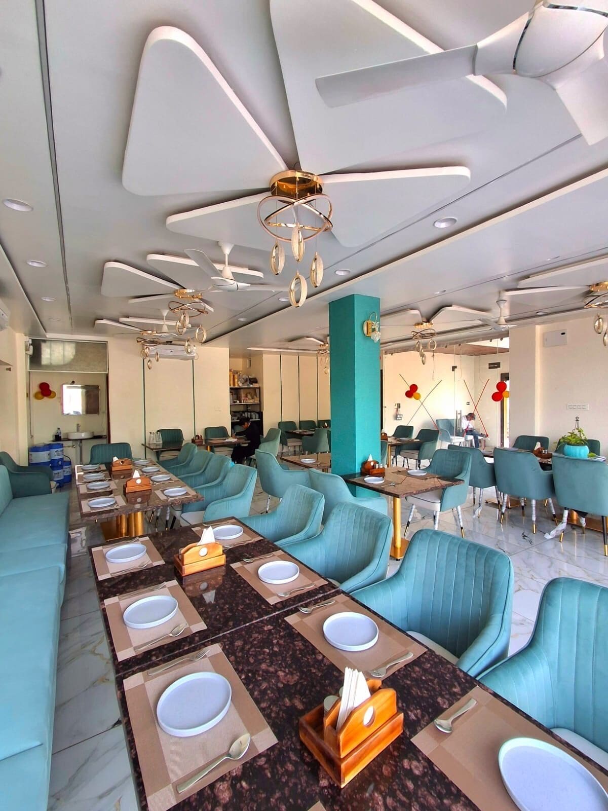 A modern dining area with teal chairs, marble tables, and contemporary ceiling fixtures.