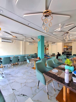 A modern restaurant interior with marble flooring, teal upholstered seating, and contemporary ceiling fans. - Rajguru Guest House (Ujjain)