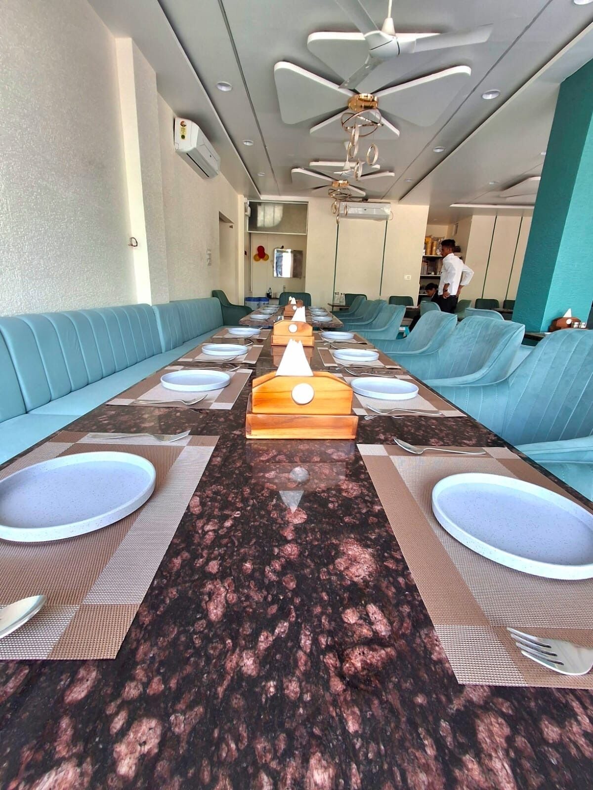A conference room with a long table, blue cushioned seating, ceiling fans, and a modern design.