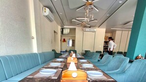 Un salón de conferencias con una larga mesa, asientos acolchados azules, ventiladores de techo y un diseño moderno.