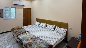 Un dormitorio con cama, ventilador de techo, equipo de aire acondicionado, armario de madera y una pequeña mesa con silla.