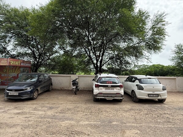 A parking area with three cars and a motorcycle, surrounded by trees and a concrete wall.
